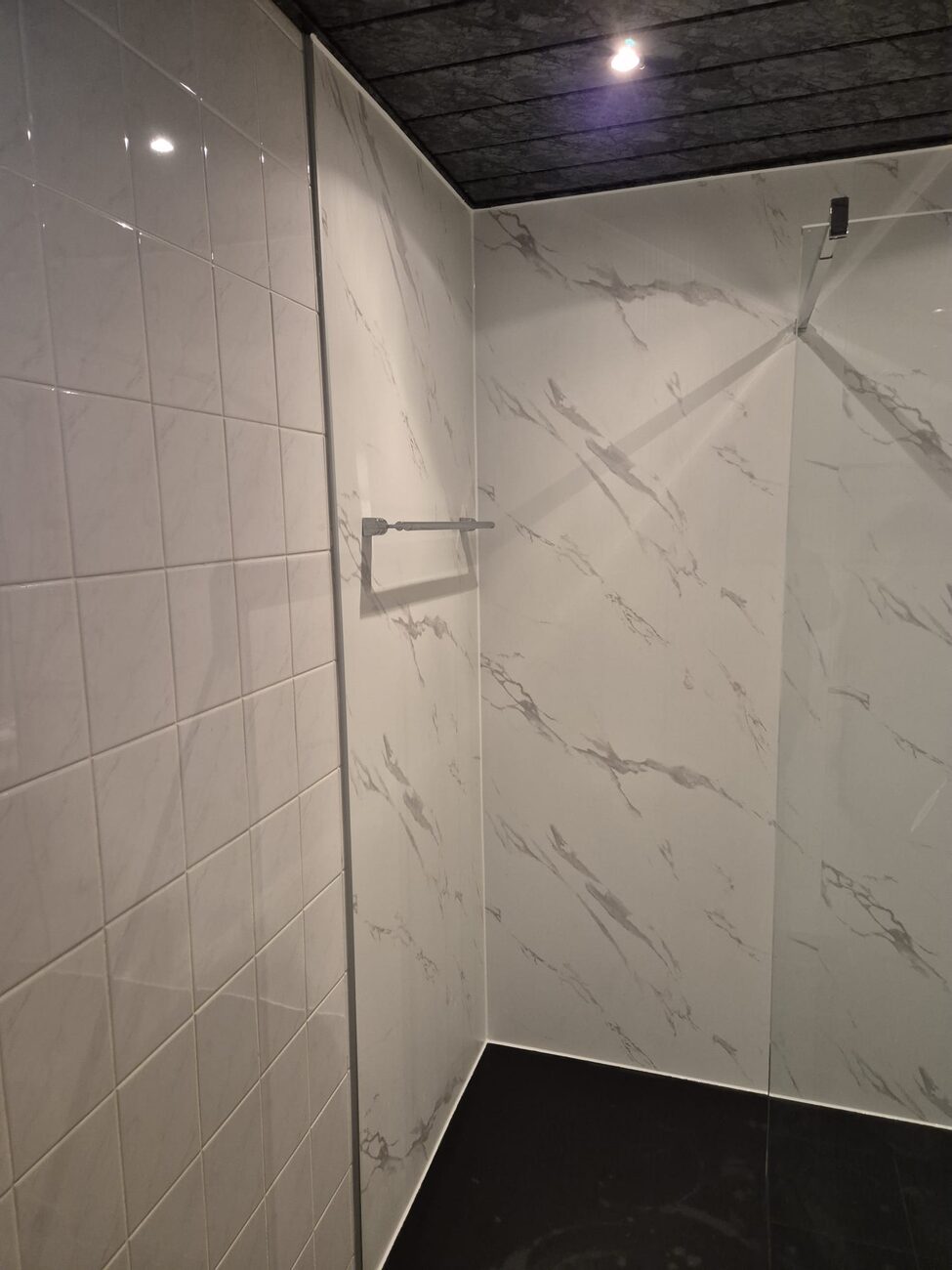 Gerenoveerde badkamer met witte tegels, marmerlook wandpanelen en donkere vloer.