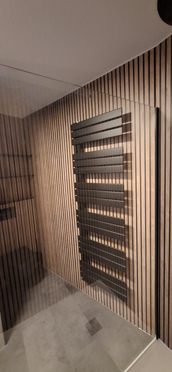 Moderne badkamer met houten lattenwand, donkere handdoekradiator en glazen douchewand.