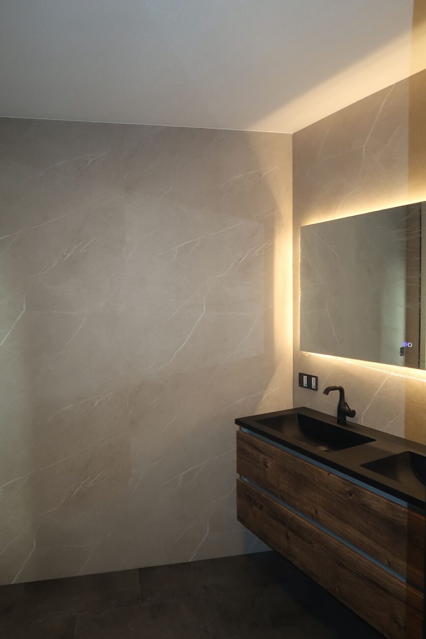 Moderne badkamer met houten wastafelmeubel, zwarte wasbakken en verlichte spiegel.