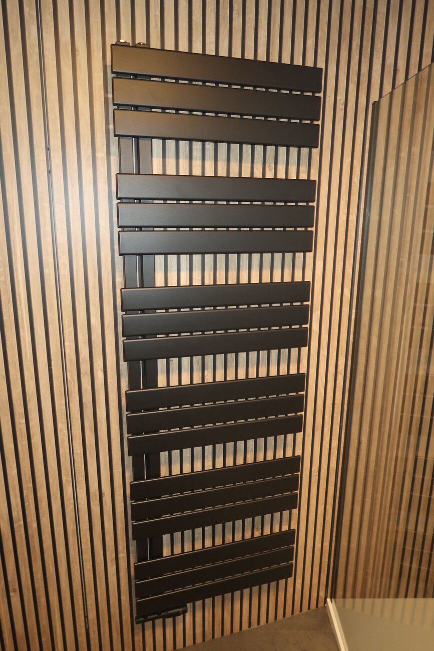 Zwarte designradiator op houten lattenwand in badkamer