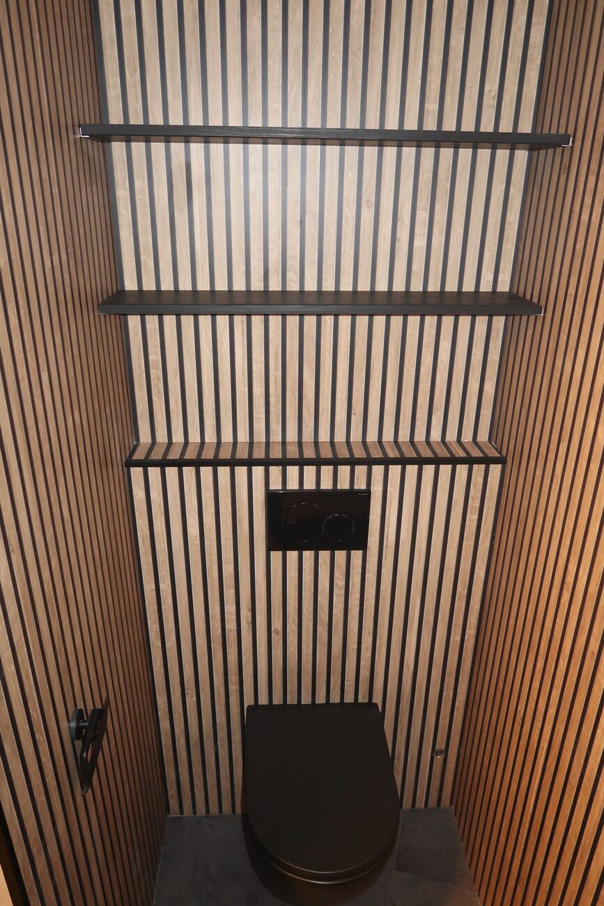 Toiletruimte met houten lattenwanden, zwarte toiletpot en planken