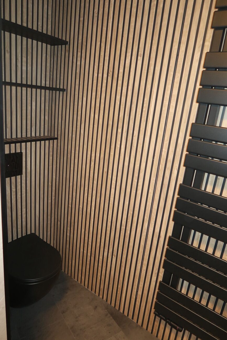 Toiletruimte met houten lattenwand, zwart toilet en zwarte handdoekradiator