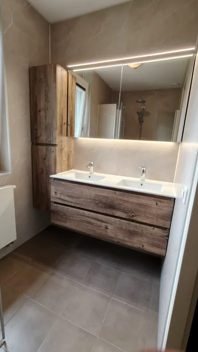 Dubbel wastafelmeubel in houtlook met ledspiegel en hoge kast, beige marmerlook wandpanelen en grijze vloer