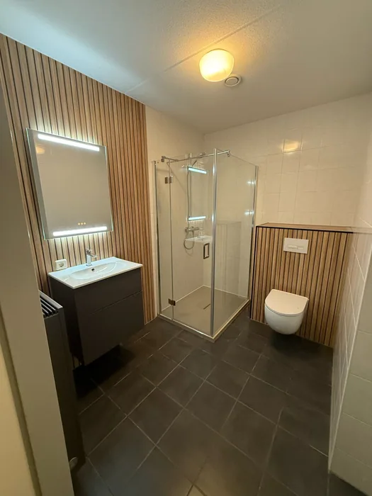 Complete badkamer met houten lamellen, led-spiegel, douchecabine, hangtoilet en donkere vloer