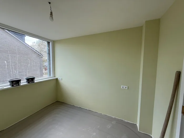 Lege kamer met lichtgroene muren, groot raam en kale dekvloer