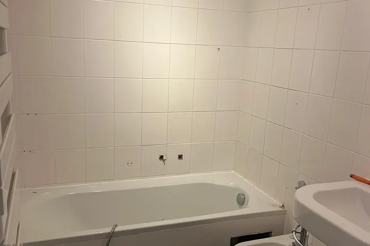 Witte getegelde badkamer met ligbad, hangend bidet en wastafel, sloop net gestart