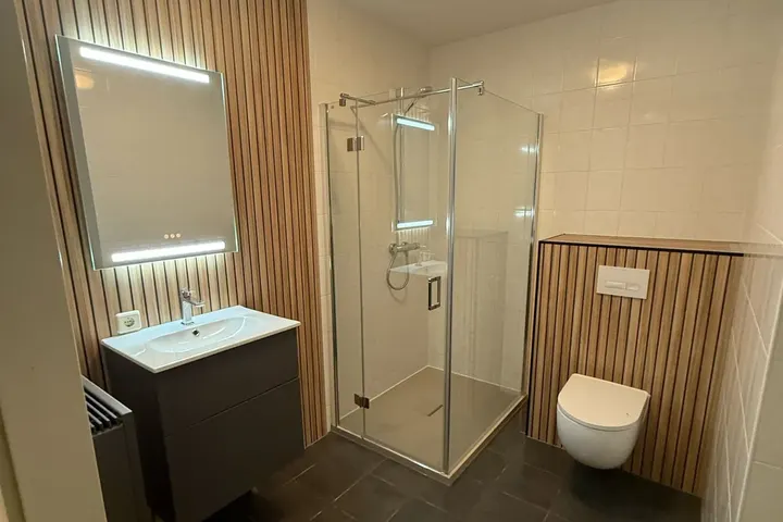 Complete badkamer met houten lamellen, led-spiegel, douchecabine, hangtoilet en donkere vloer