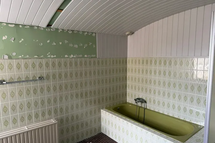 Gedateerde badkamer met groen ligbad, groen-wit motieftegels en schrootjesplafond