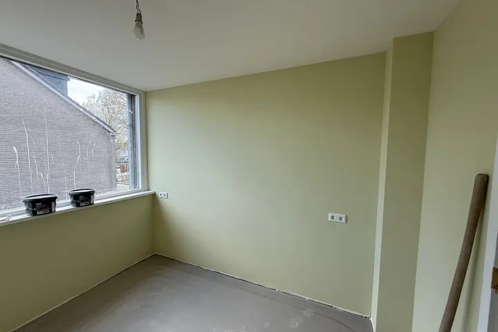 Lege kamer met lichtgroene muren, groot raam en kale dekvloer