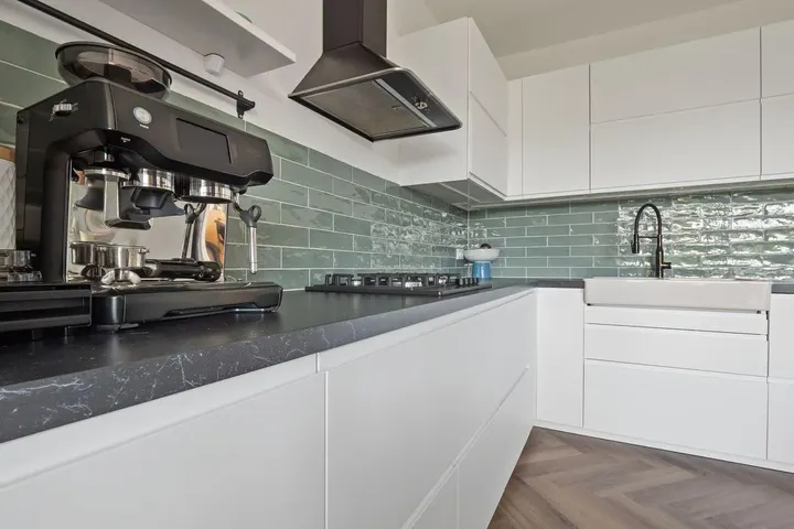 Detail keuken met zwart aanrechtblad, groene wandtegels en afzuigkap