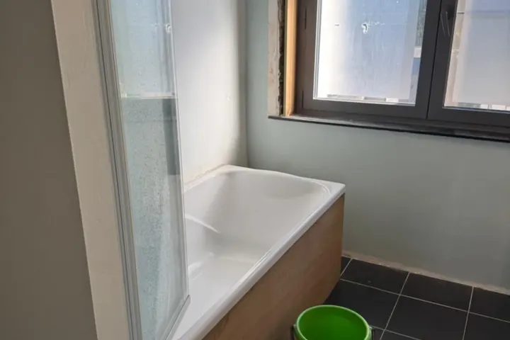 Oude badkamer met ligbad en badwand onder raam, zwarte vloertegels