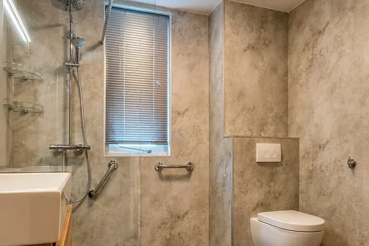 Seniorvriendelijke badkamer met drempelloze inloopdouche, steunbeugels, hangtoilet en steenlook wandpanelen