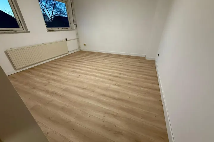 Lege slaapkamer met radiator, witte muren en lichte laminaatvloer