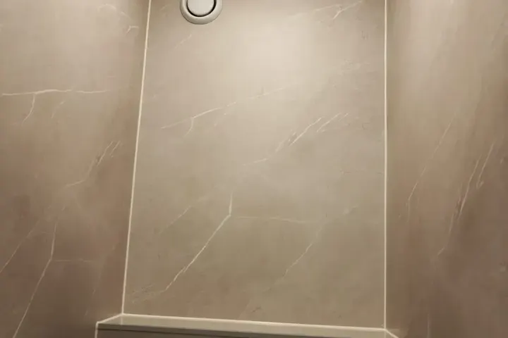 Toiletruimte met beige marmerlook wandpanelen, voorzetwand met bedieningsplaat en ventilatierooster