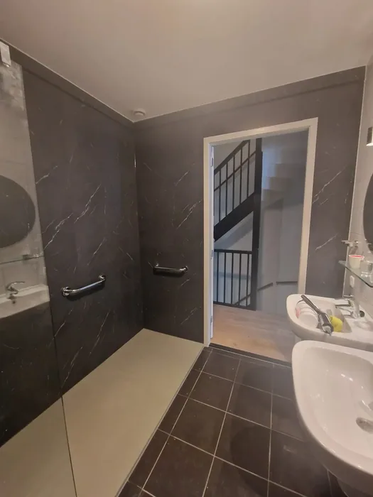 Badkamer met antraciet marmerlook panelen, inloopdouche, steunbeugels en twee wastafels