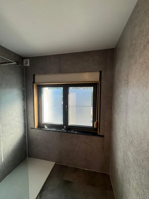 Badkamer rondom bekleed met grijze steenlook wandpanelen, raam en inloopdouche met witte douchebak