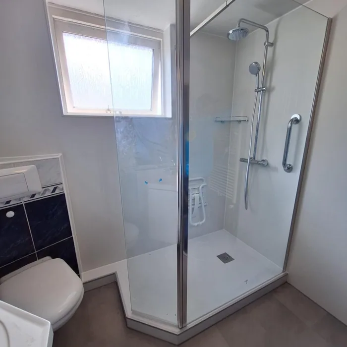 Glazen douche met witte panelen, regendouche, steunbeugel en opklapzitje, naast een hangtoilet