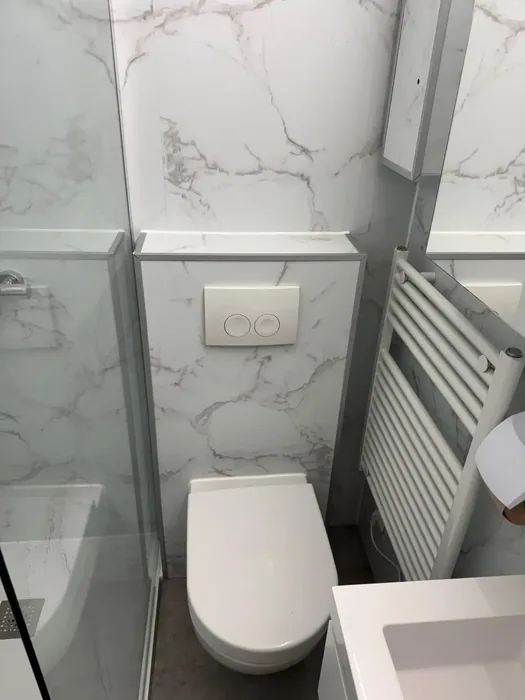 Wit hangtoilet op voorzetwand met witte marmerlook wandpanelen en witte handdoekradiator