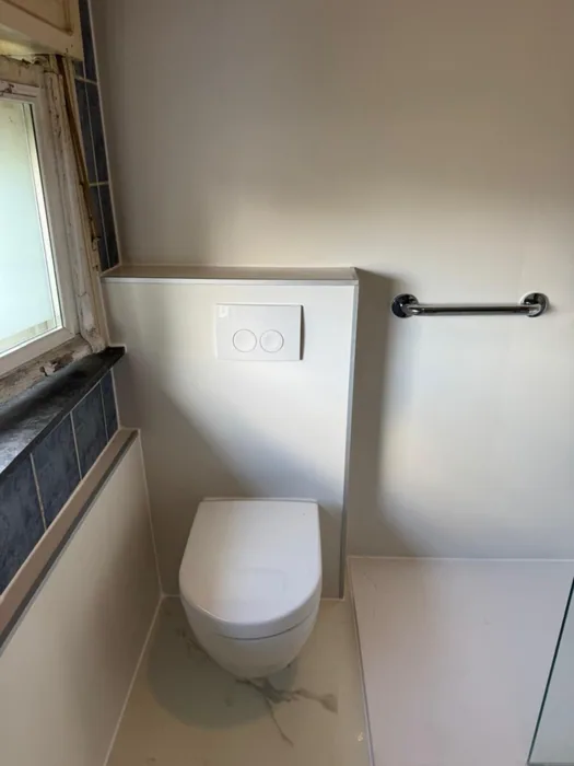 Hangtoilet tegen witte voorzetwand met bedieningsplaat, steunbeugel en vloer in marmerlook