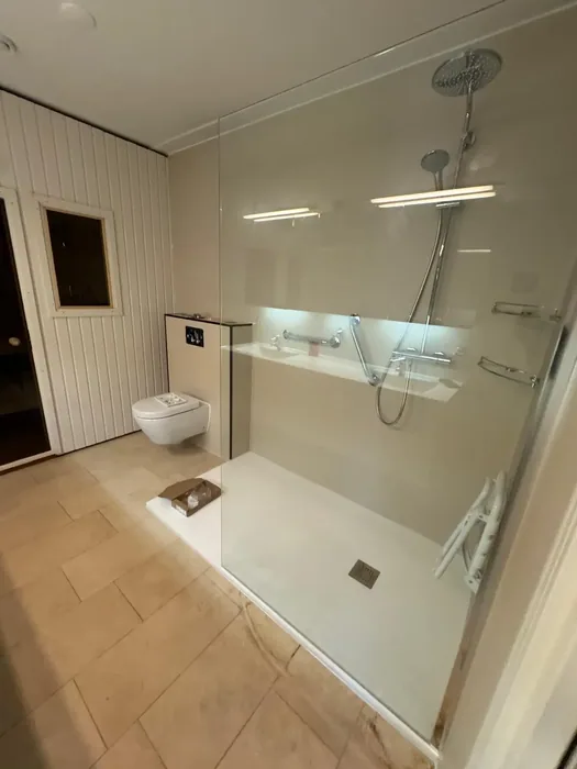 Ruime inloopdouche met glazen wand, douchezitje, steunbeugels, verlichte nis en hangtoilet