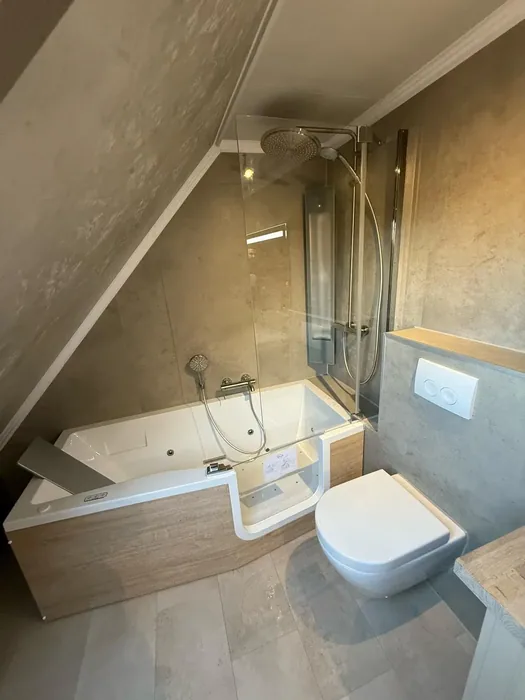 Zolderbadkamer met instapbad met deur, badwand, regendouche, hangtoilet en steenlook wandpanelen
